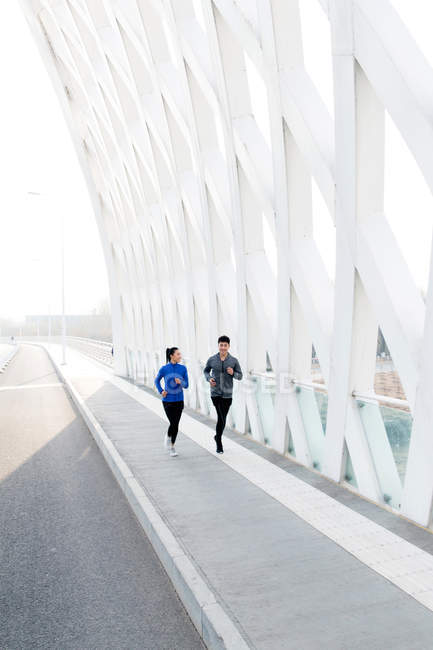 Young couple of joggers in sportswear training together on bridge — Stock Photo