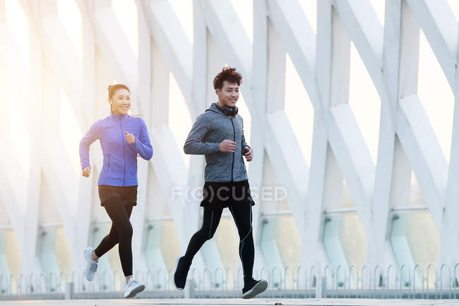 Vue pleine longueur de sourire jeunes coureurs asiatiques formation ensemble en plein air — Photo de stock