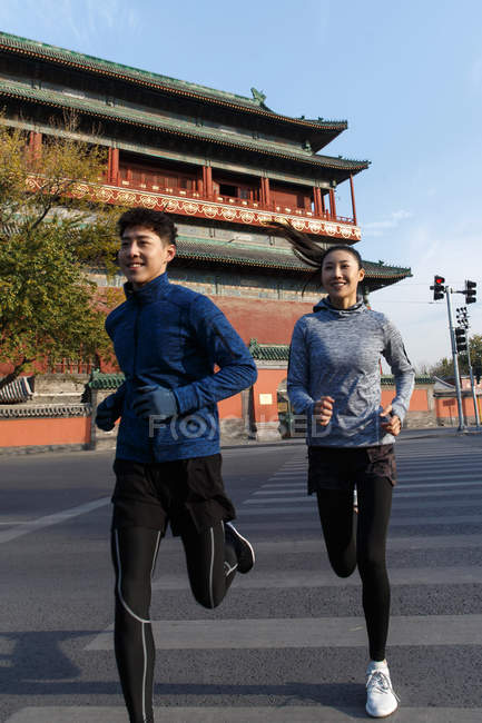 Sonriendo jóvenes atletas masculinos y femeninos trotando juntos calle - foto de stock