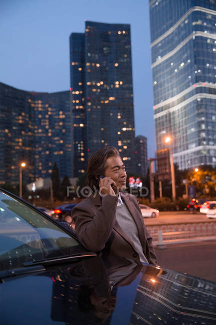 Счастливый взрослый мужчина разговаривает по смартфону и смотрит вдаль в ночном городе — стоковое фото