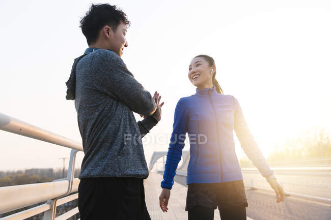 Низький кут зору молодих азіатських бігунів, що тягнуться разом під час тренування на мосту вранці — стокове фото