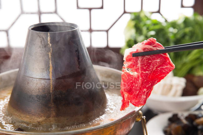 Primo piano vista di bacchette con carne sopra pentola di rame caldo, concetto piatto sfregamento — Foto stock
