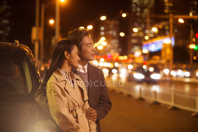 Happy asian couple standing near car at evening — Stock Photo