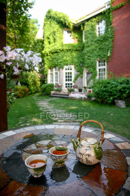 Vista de perto do conjunto de chá cerâmico com chaleira e xícaras na mesa no quintal — Fotografia de Stock