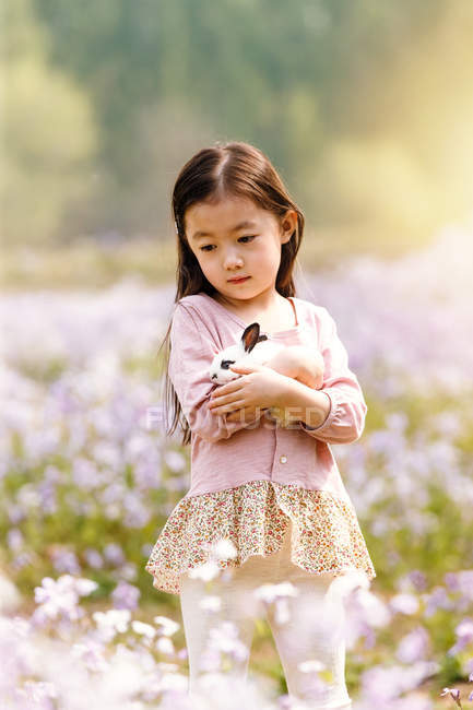 Adorable asian kid in dress holding rabbit at flower field — Stock Photo