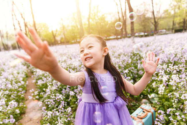 Adorable asiatique enfant dans robe attraper savon bulles à fleur champ — Photo de stock