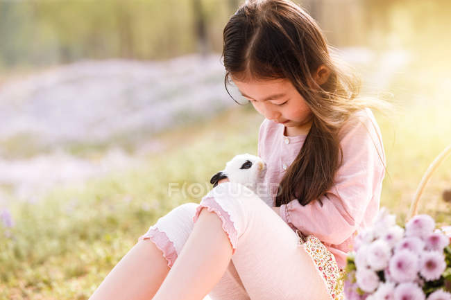 Adorável asiático criança no vestido segurando coelho no flor campo — Fotografia de Stock