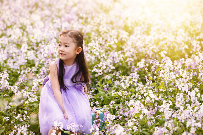 Entzückende asiatische Kind im Kleid sitzt auf Tasche auf Blumenfeld — Stockfoto