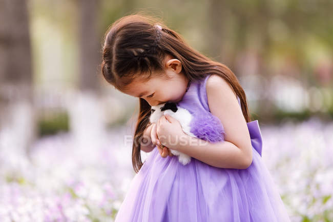 Adorable asian kid in dress holding rabbit at flower field — Stock Photo
