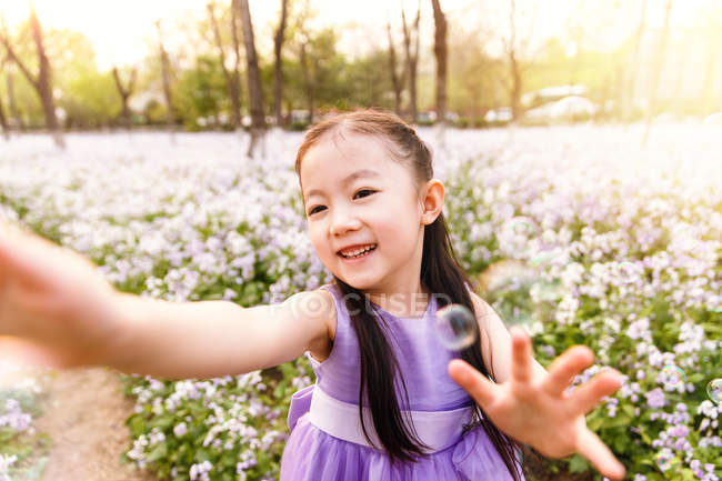 Adorável asiático criança no vestido captura sabão bolhas no flor campo — Fotografia de Stock