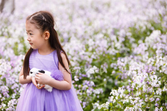 Entzückendes asiatisches Kind im Kleid mit Kaninchen auf dem Blumenfeld — Stockfoto