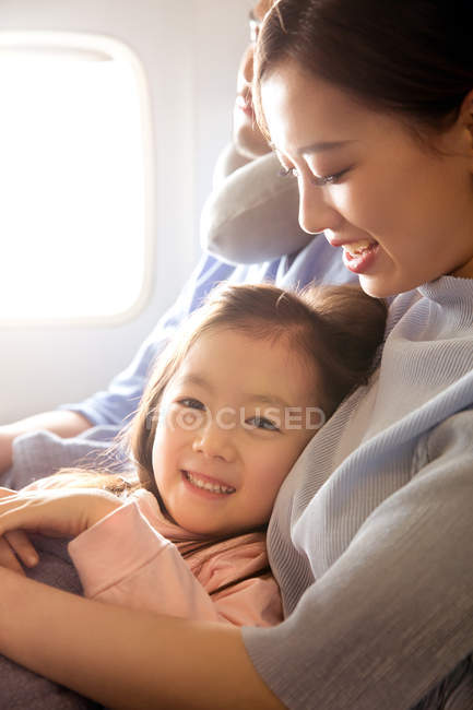 Famille heureuse avec un enfant voyageant en avion, fille souriant à la caméra — Photo de stock