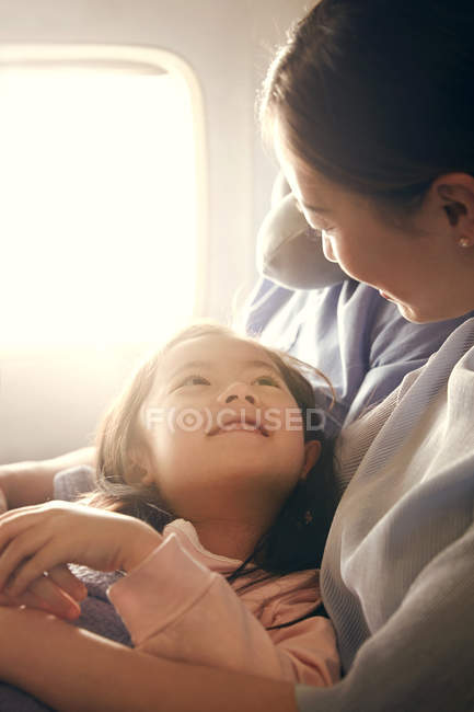 Щаслива сім'я з однією дитиною, що подорожує літаком, дівчина дивиться на матір — стокове фото