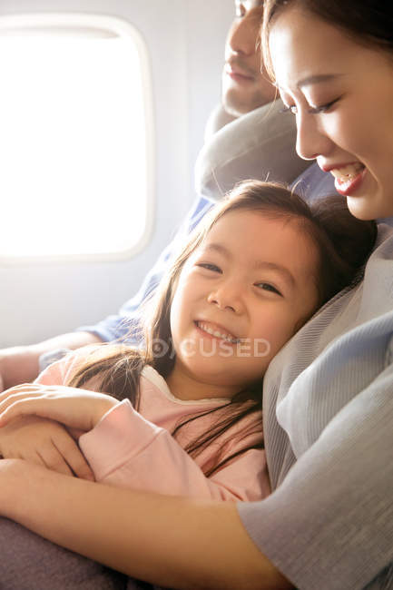 Famille heureuse avec un enfant voyageant en avion, fille souriant à la caméra — Photo de stock