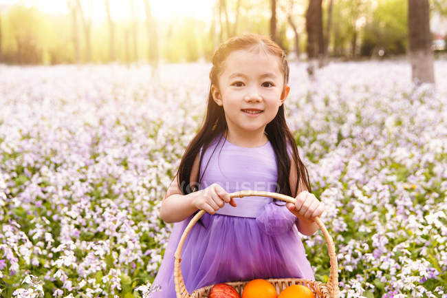 Чарівні азіатських дитина в одязі тримає кошик з пасхальні яйця в полі квітки — стокове фото
