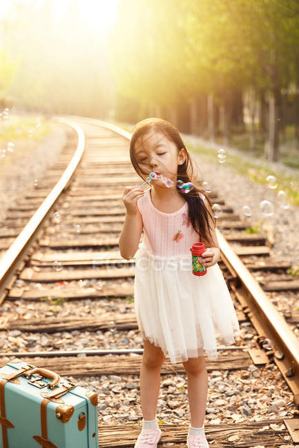 Adorable asian kid blowing soap bubbles near railroad — Stock Photo