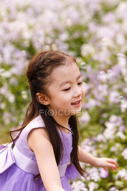 Adorável asiático criança no vestido captura sabão bolhas no flor campo — Fotografia de Stock