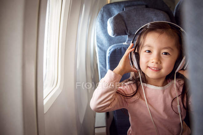 Entzückendes glückliches Kind mit Kopfhörern, das im Flugzeug sitzt und in die Kamera lächelt — Stockfoto
