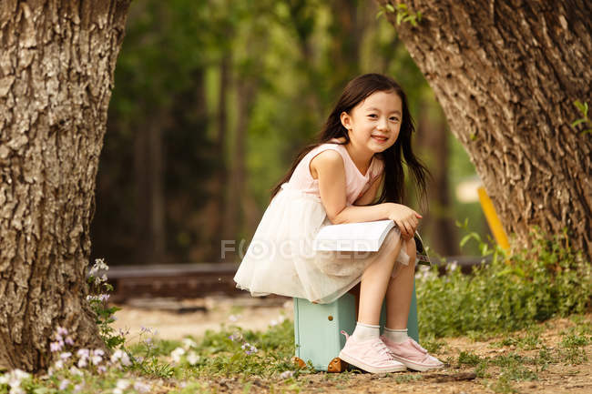 Очаровательный азиатский ребенок сидит на дорожной сумке — стоковое фото