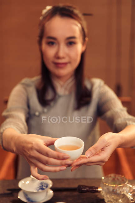 Belle jeune asiatique femme tenant tasse de thé et souriant à caméra — Photo de stock