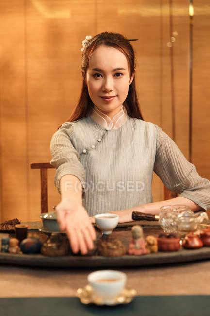 Hermosa joven asiático mujer mostrando taza de té y sonriendo en cámara - foto de stock