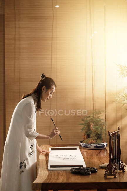 Side view of young asian woman holding brush and writing chinese  characters — Stock Photo
