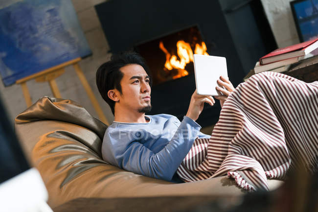 Focused young asian man sitting on bean bag chair and using digital tablet at home — Stock Photo