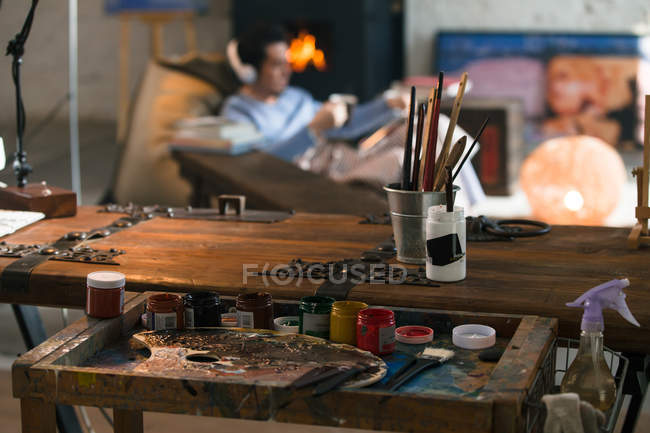 Primo piano vista di strumenti d'arte e giovane uomo in cuffia seduto vicino al camino — Foto stock