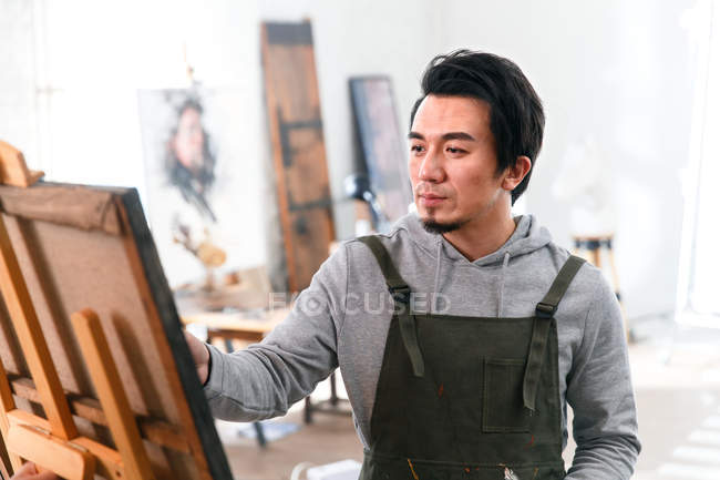 Enfocado joven asiático artista en delantal pintura cuadro en arte estudio - foto de stock