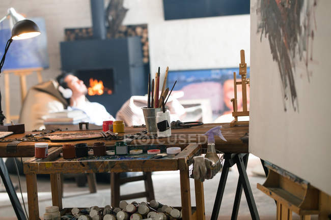 Close-up view of art tools and young man in headphones sitting near fireplace — Stock Photo
