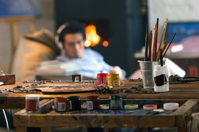 Nahaufnahme von Kunstwerkzeugen und einem jungen Mann mit Kopfhörern, der am Kamin sitzt — Stockfoto