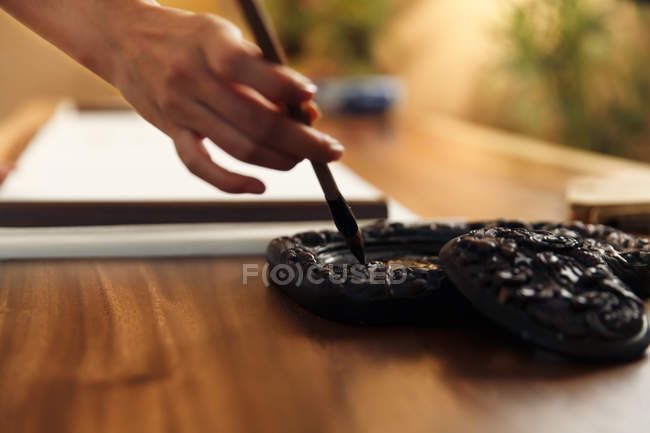 Vista parcial de cerca de la mujer poniendo cepillo de caligrafía en la tinta - foto de stock