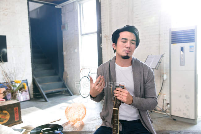 Красивий азіатський чоловік тримає акустичну гітару вдома — стокове фото