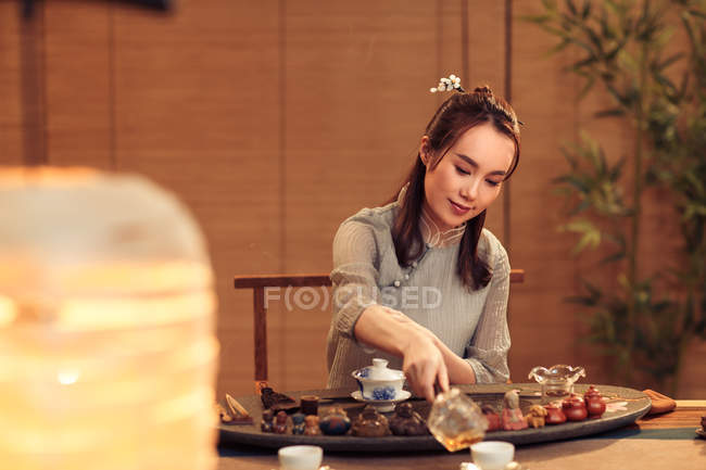 Красива усміхнена молода китайська жінка вливає чай у чашку — стокове фото