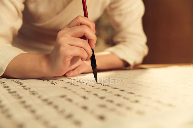 Primo piano vista parziale della donna che tiene pennello calligrafia e scrittura caratteri cinesi — Foto stock