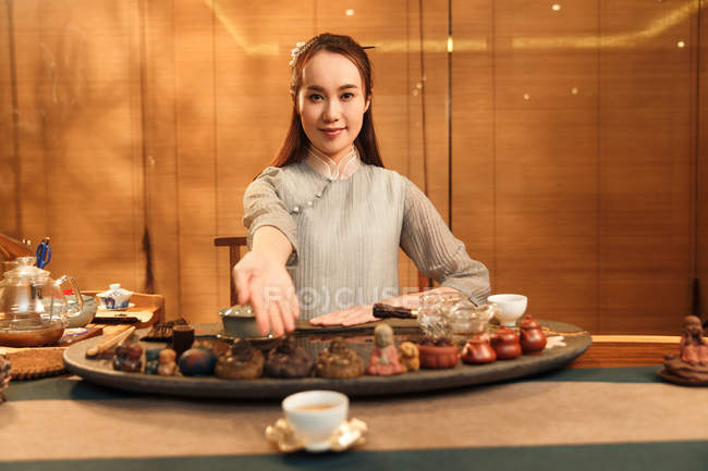 Schöne junge asiatische Frau zeigt Tasse Tee und lächelt in die Kamera — Stockfoto