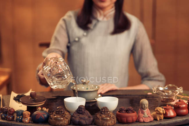Tiro recortado de la mujer vertiendo agua en tazas durante la ceremonia del té chino - foto de stock