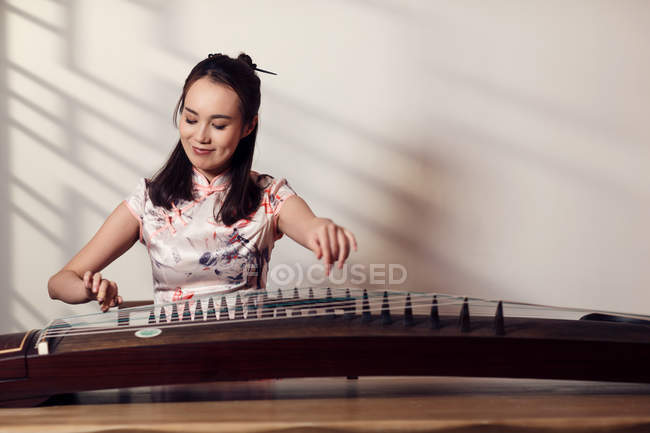 Sorrindo jovem asiático mulher jogar tradicional chinês guzheng corda instrumento — Fotografia de Stock