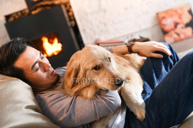 Guapo relajado asiático hombre abrazando perro y descansando en frijol bolsa silla en casa - foto de stock