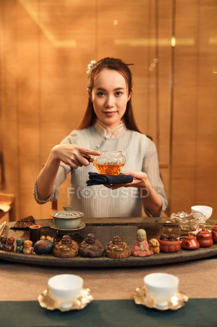 Beautiful young asian woman holding glass container with tea and looking at camera — Stock Photo