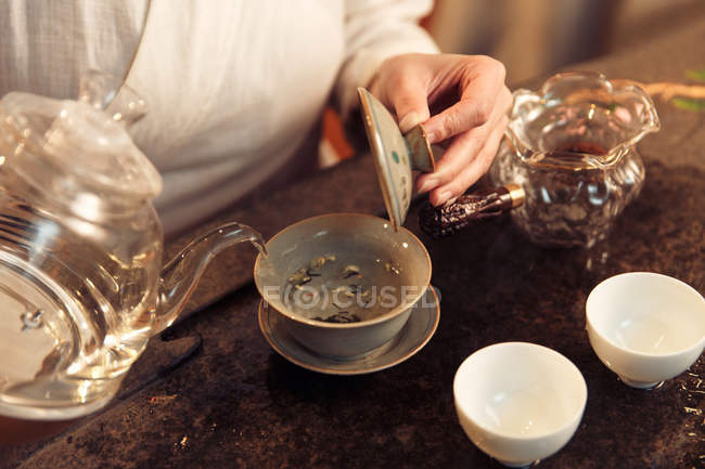 Abgeschnittene Aufnahme einer Frau, die eine Teekanne hält und Wasser in ein Porzellangefäß gießt — Stockfoto