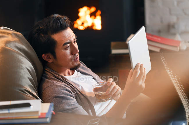 Fokussierter asiatischer Mann mit Glas Whiskey und digitalem Tablet zu Hause — Stockfoto