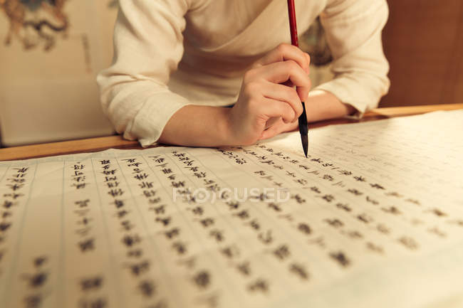 Tiro recortado de mulher segurando escova de caligrafia e escrever caracteres chineses — Fotografia de Stock