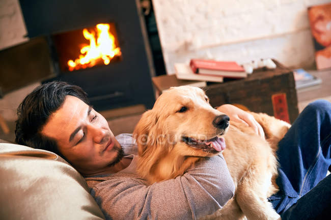 Handsome asian man sitting in bean bag chair and hugging dog at home — Stock Photo