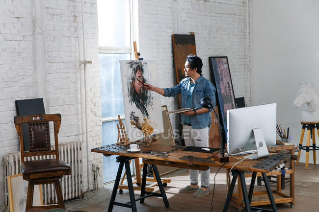 Фокусований чоловічий художник у фартусі, що тримає палітру та портрет живопису в студії — стокове фото