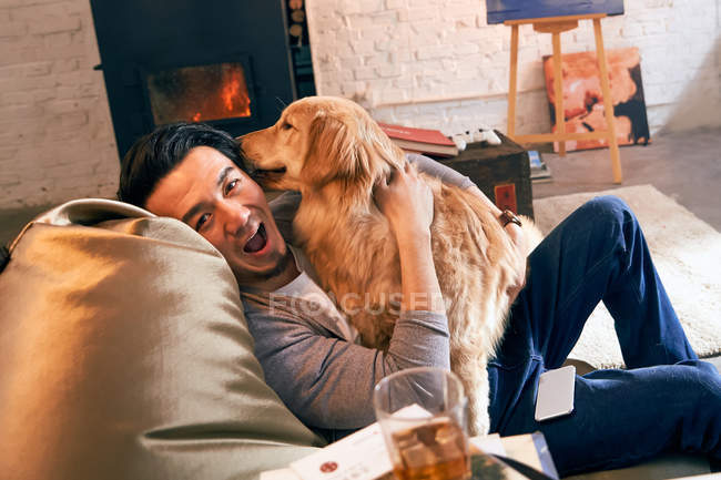 Счастливый мужчина играет с собакой и улыбается на камеру дома — стоковое фото