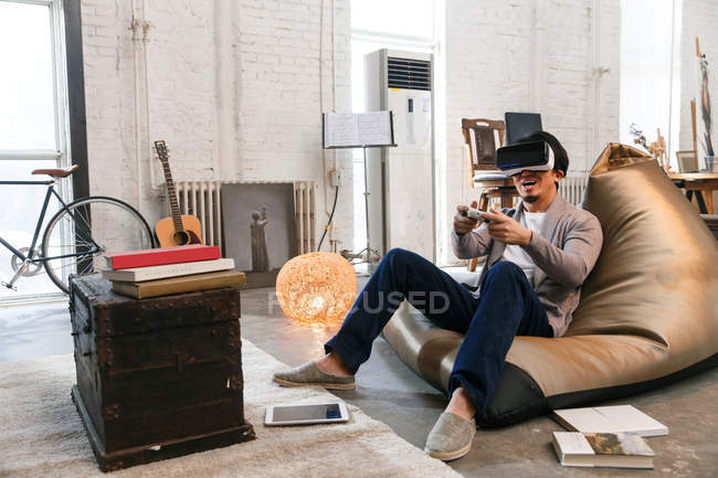 Aufgeregter junger Mann in Virtual-Reality-Headset spielt zu Hause mit Gamepad — Stockfoto