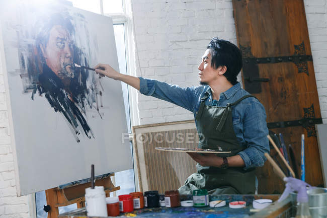 Artista masculino concentrado en delantal pintura retrato en el estudio - foto de stock