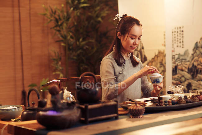 Красива усміхнена молода китайка тримає порцеляновий посуд і робить чай — стокове фото