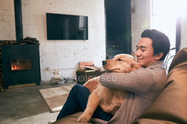 Вид сбоку счастливого человека, сидящего на стуле из фасоли и играющего с собакой дома — стоковое фото